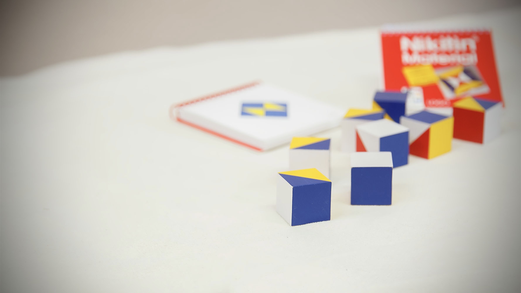 Bunte Würfel mit gelben, blauen und weißen Flächen liegen auf einem hellen Tisch